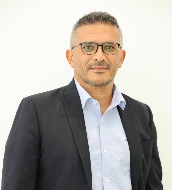 Ihab Sakr, Design Manager, Trojan Property Investment (TPI) - Man in a black suit and glasses with a light blue shirt standing against a white background looking confidently at the camera. Professional business portrait.