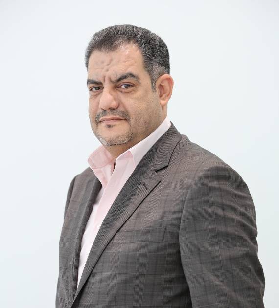Yehia Aboushanab, Project Manager, Trojan Property Investment (TPI) - Man in a grey suit and pink shirt looks confidently at the camera with a neutral background highlighting his professional attire and calm demeanour.